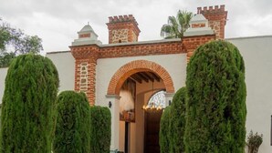 A courtyard with a brick entrance, a stone pathway, and neatly trimmed topiary trees. - Hotel Ex hacienda Chautla Puebla, Trademark by Wyndham (San Salvador el Verde)