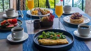 A table set with breakfast items, including pancakes, a fruit salad, and coffee, overlooking a forested area. - Hotel Ex hacienda Chautla Puebla, Trademark by Wyndham (San Salvador el Verde)