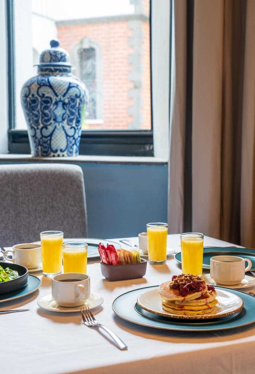 A breakfast table with pancakes, orange juice, coffee, and a bowl of fruit.