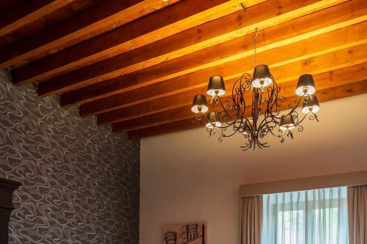 Ein Schlafzimmer mit Holzbalkendecke, einem Bett mit weißer Bettwäsche, einer Wand mit Muster und einem großen Fenster mit Vorhängen.