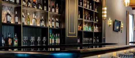 Una zona de bar con estantes llenos de botellas y vasos, una barra curva y taburetes.