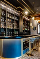 Una zona de bar con estantes llenos de botellas y vasos, una barra curva y taburetes.