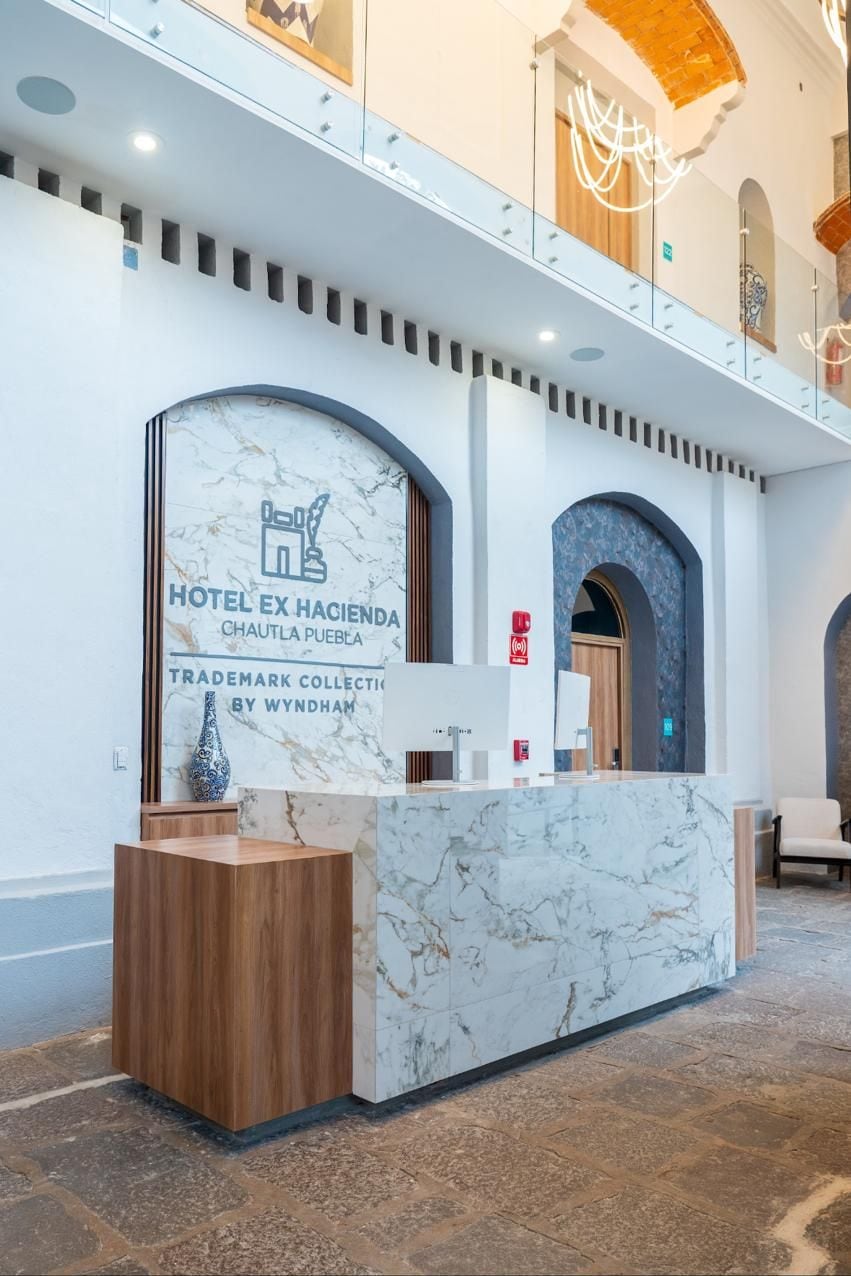 A hotel reception desk with a marble counter and a wooden base, a sign indicating it's Hotel Ex Hacienda, and a trademark collection by Wyndham.
