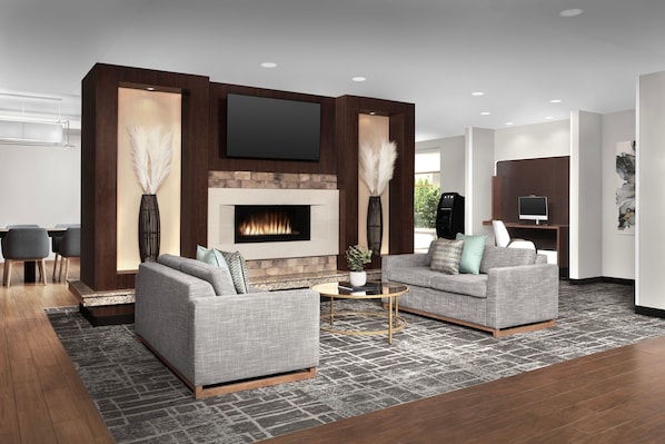 A modern living room with two grey sofas, a fireplace, a flat-screen TV, and a reception desk.