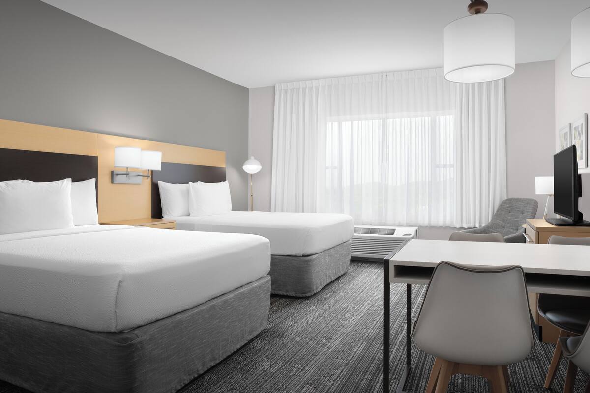 A hotel room with two beds, a desk, a chair, and a television.