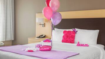 Habitación de hotel con una cama bien hecha, una mesita de noche con lámpara, teléfono y un cojín decorativo rosa.
