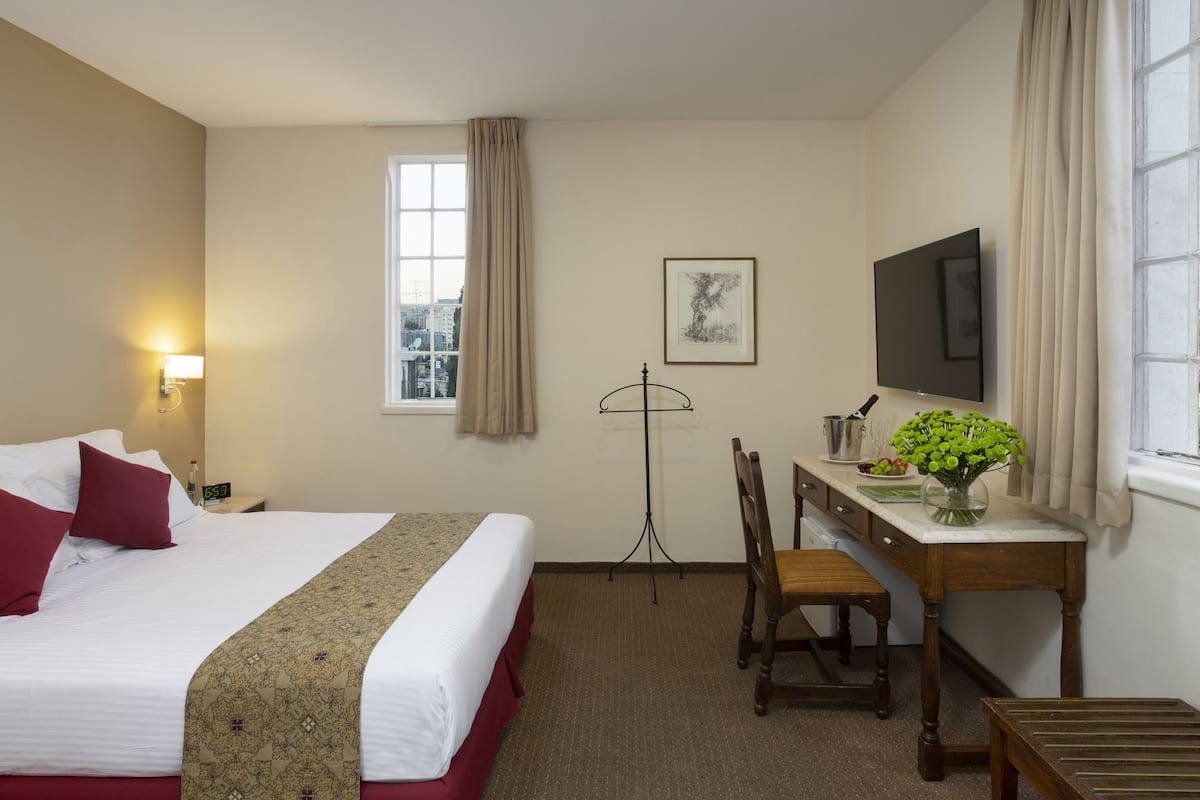 Une chambre d’hôtel équipée d’un lit, d’un bureau, d’une chaise, d’une télévision et d’une fenêtre avec des rideaux.