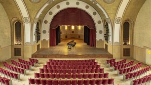 A grand hall with a stage, red chairs, and ornate ceiling designs. - YMCA Three Arches Hotel (Jerusalem)