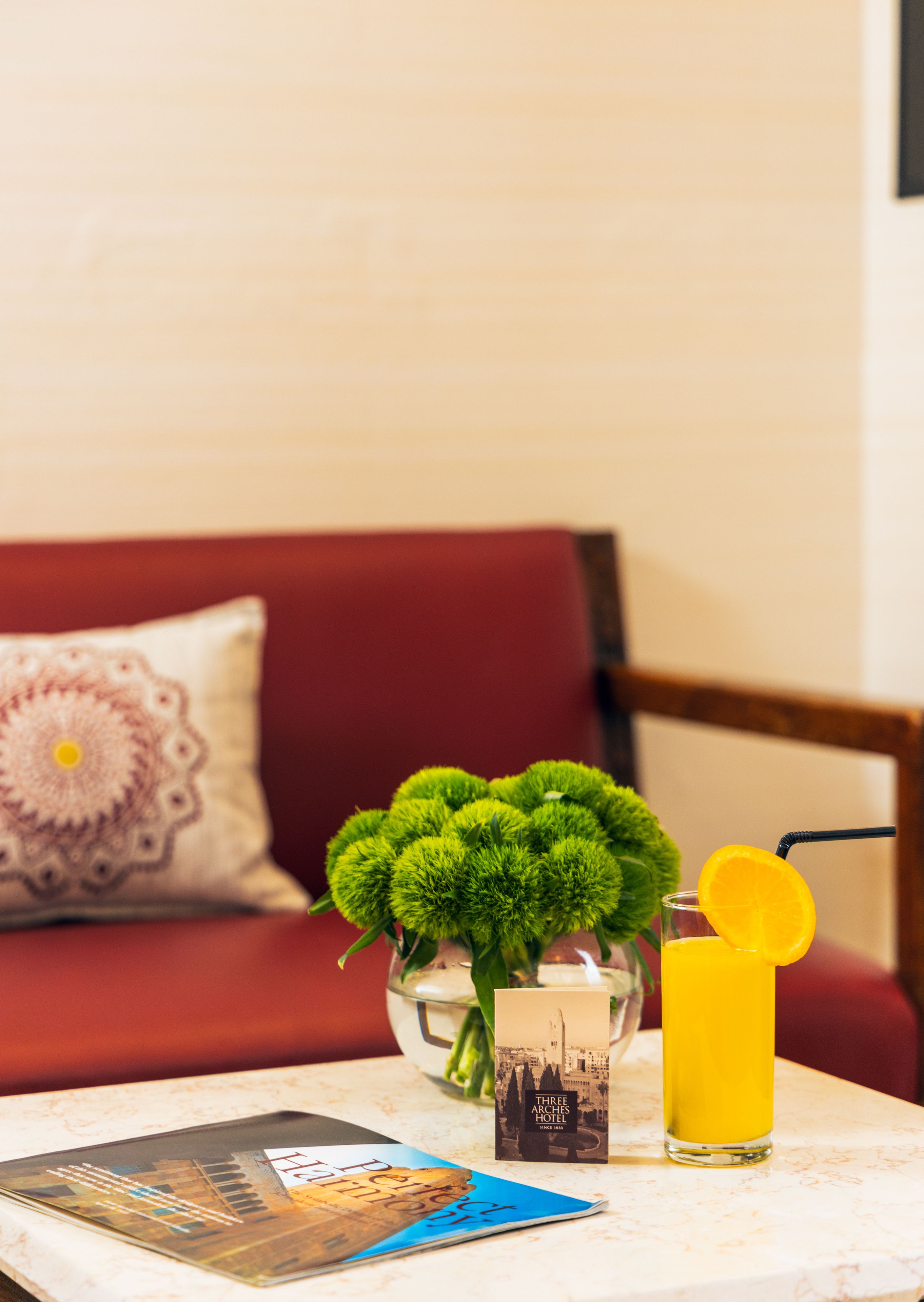 Une table avec un verre de jus d’orange, une brochure et un vase contenant des feuilles vertes.