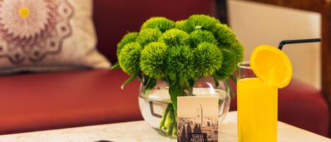 Une table avec un verre de jus d’orange, une brochure et un vase contenant des feuilles vertes.