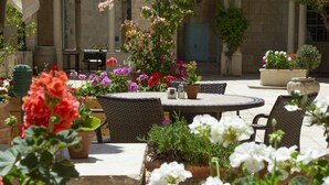 An outdoor patio area with wicker furniture, potted plants, and a stone building in the background. - YMCA Three Arches Hotel (Jerusalem)