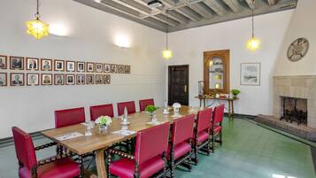 A conference room with a long wooden table, red upholstered chairs, framed portraits on the wall, and a fireplace.