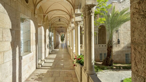 A corridor with arches, columns, and a dome in the background. - YMCA Three Arches Hotel (Jerusalem)