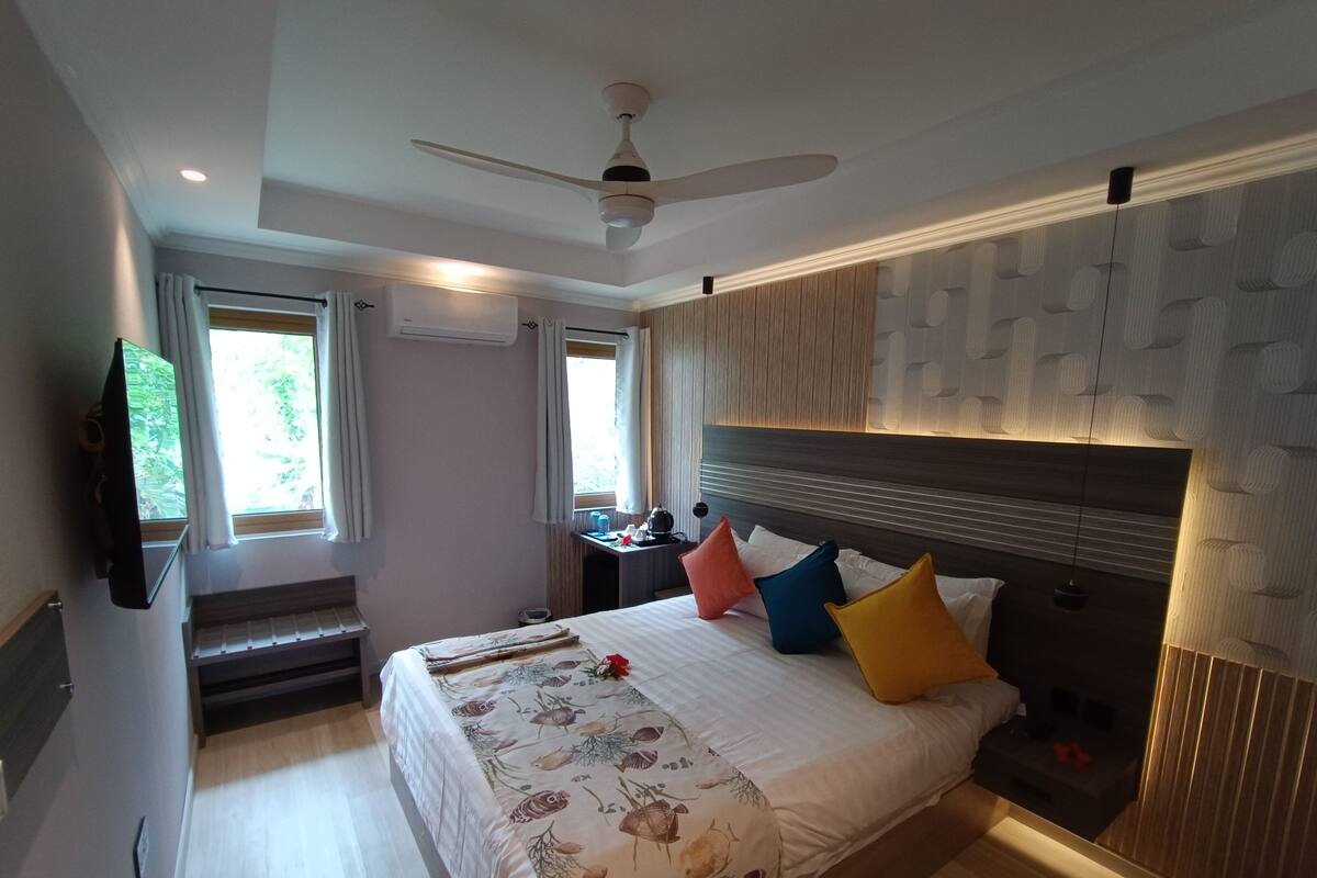 Une chambre à coucher avec un lit, un ventilateur de plafond, une télévision, un bureau et une fenêtre.
