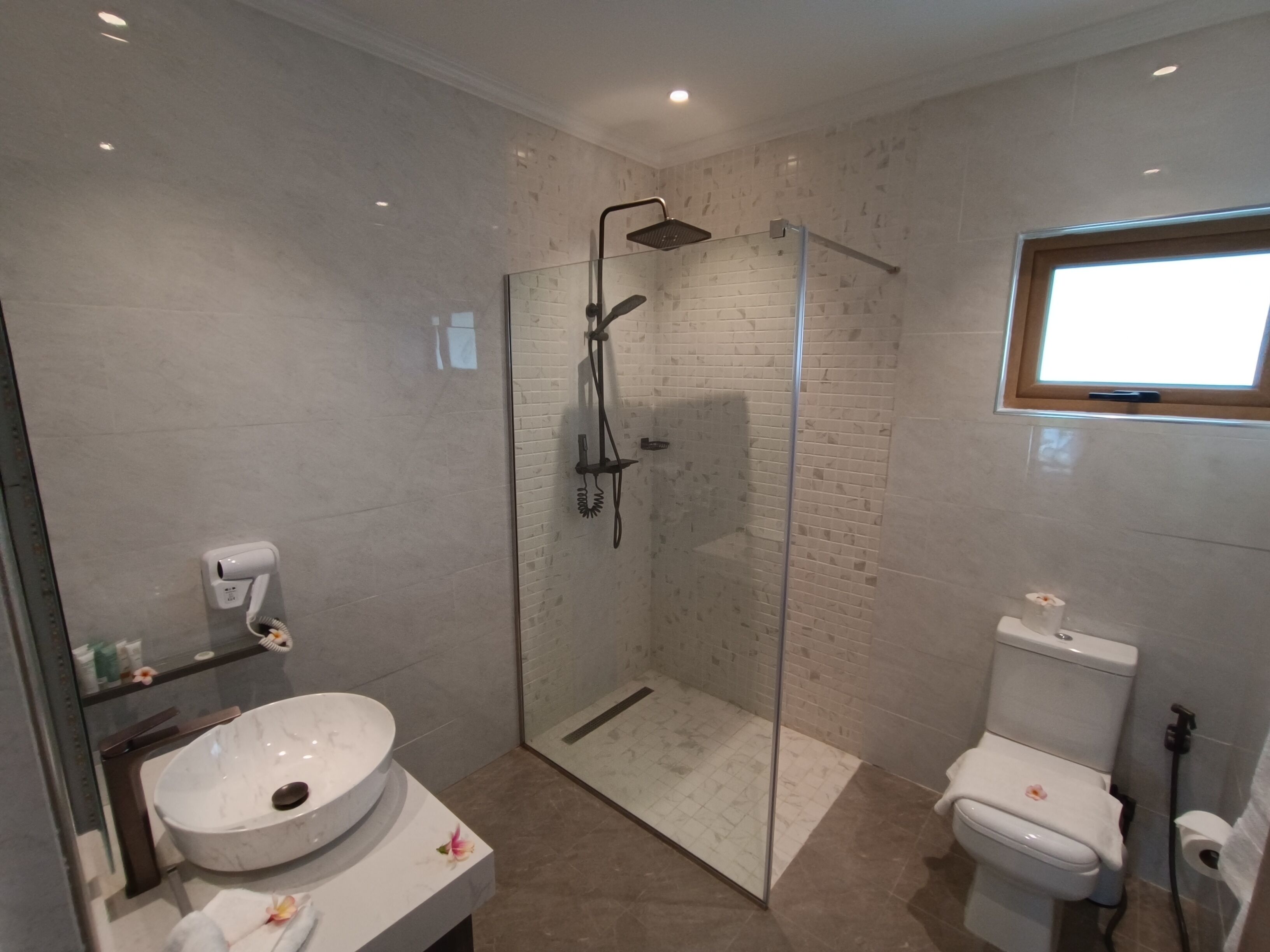 A modern bathroom with a glass-enclosed shower, a white sink with a marble basin, and a toilet.