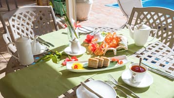 A table set with a green tablecloth, white plates, silverware, a white teapot, a white sugar bowl, a white cup, and a plate with food and flowers.