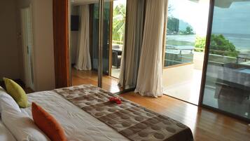 A modern hotel room with a large bed, a view of the ocean, and a balcony with outdoor furniture.