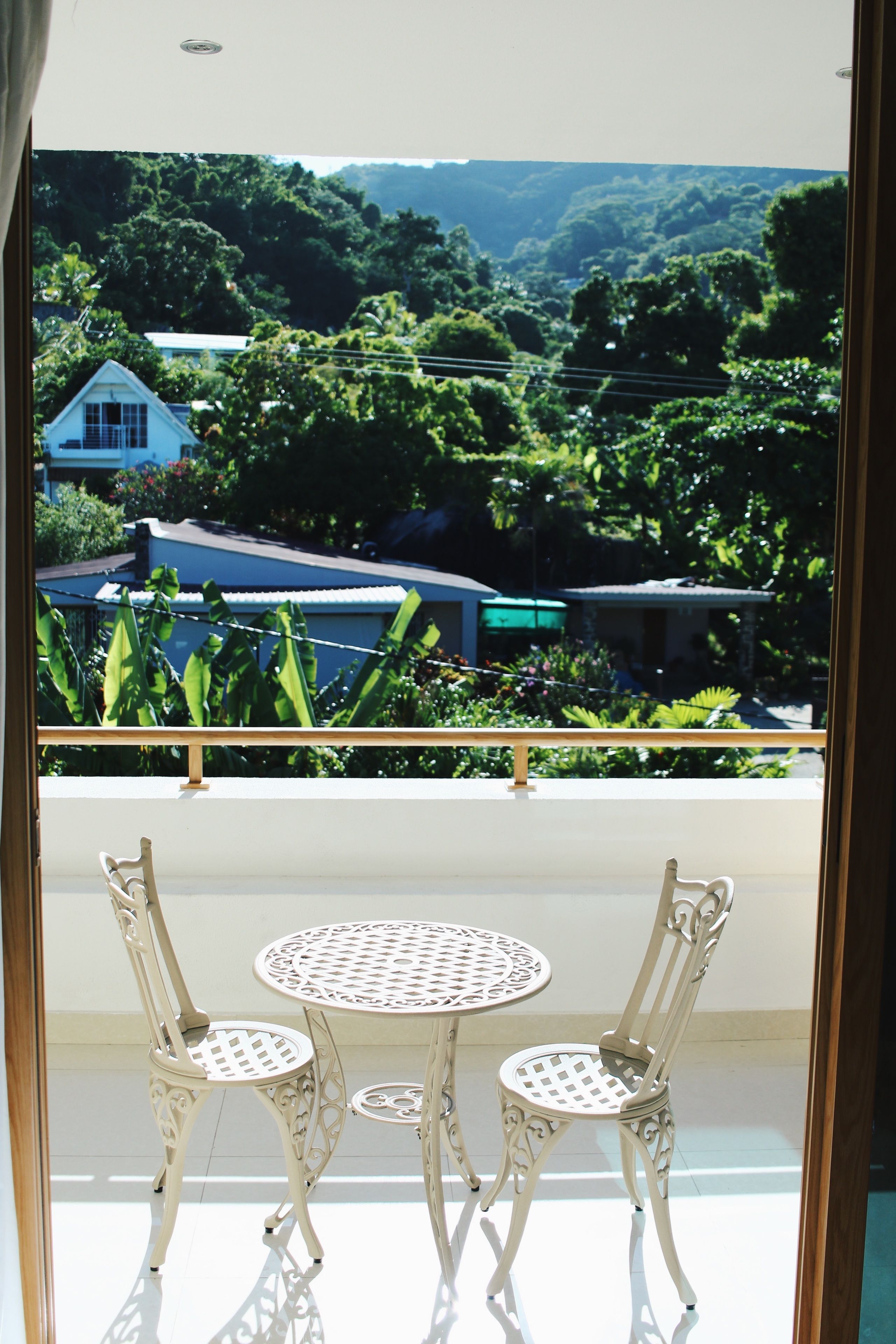A balcony with a table and two chairs, overlooking a lush green landscape with houses and trees.