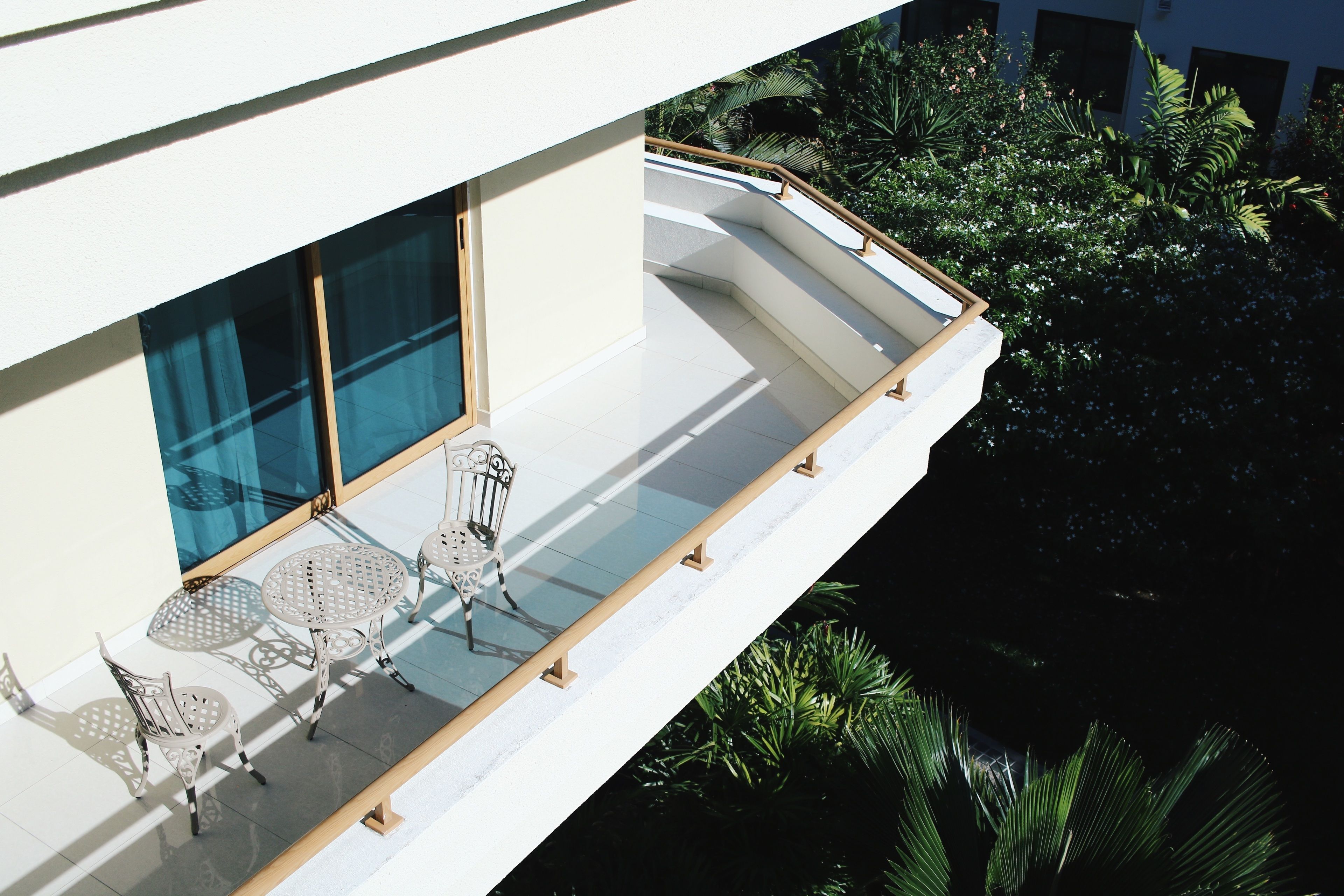 A balcony with a glass railing, two chairs, and a small table.