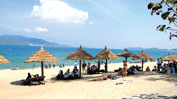 Une plage avec des parasols en chaume et des gens qui se détendent sur le sable.