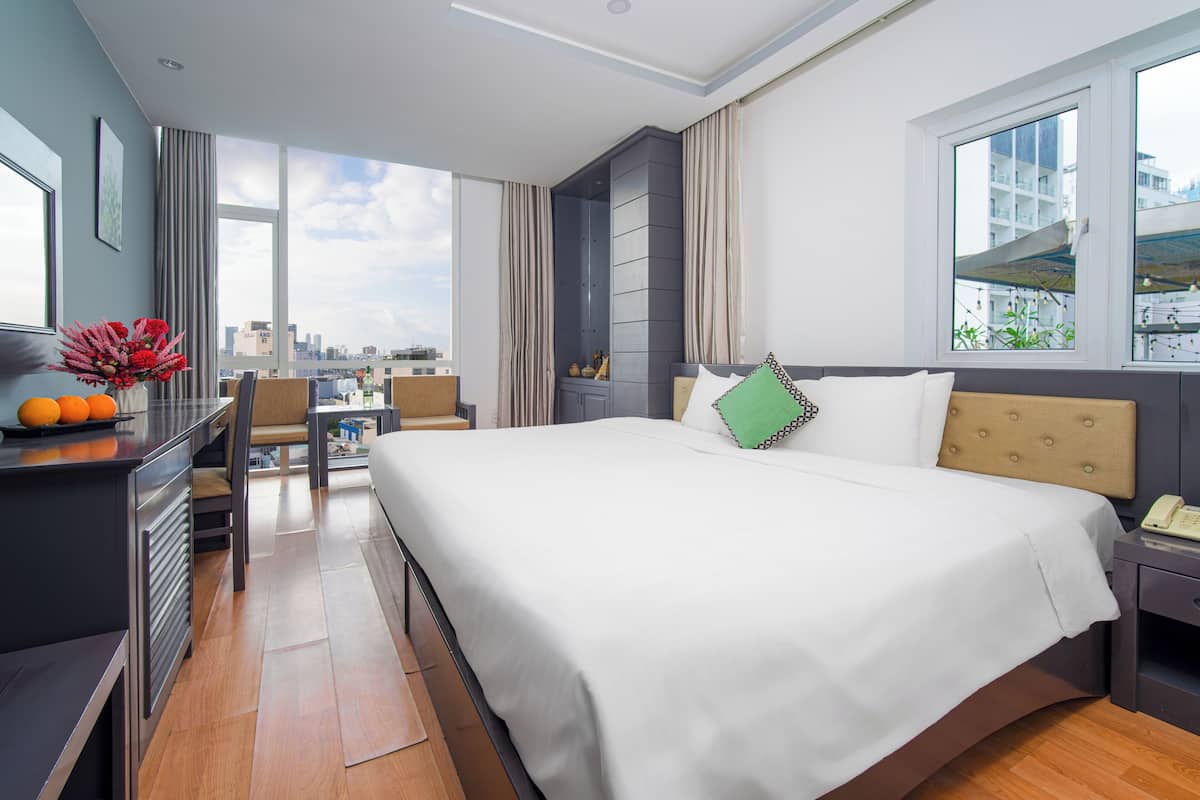A modern hotel room with a large bed, a desk, a chair, and a view of the cityscape.
