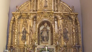 Un altar ornamentado con estatuas religiosas y una figura central, rodeado por un mostrador de mármol y un jarrón con flores.
