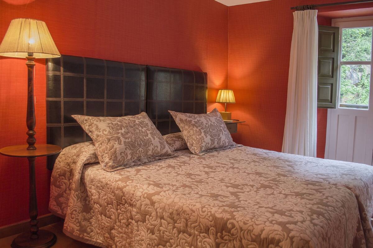 Una habitación de hotel con una cama grande, dos lámparas de noche y una ventana con cortinas.
