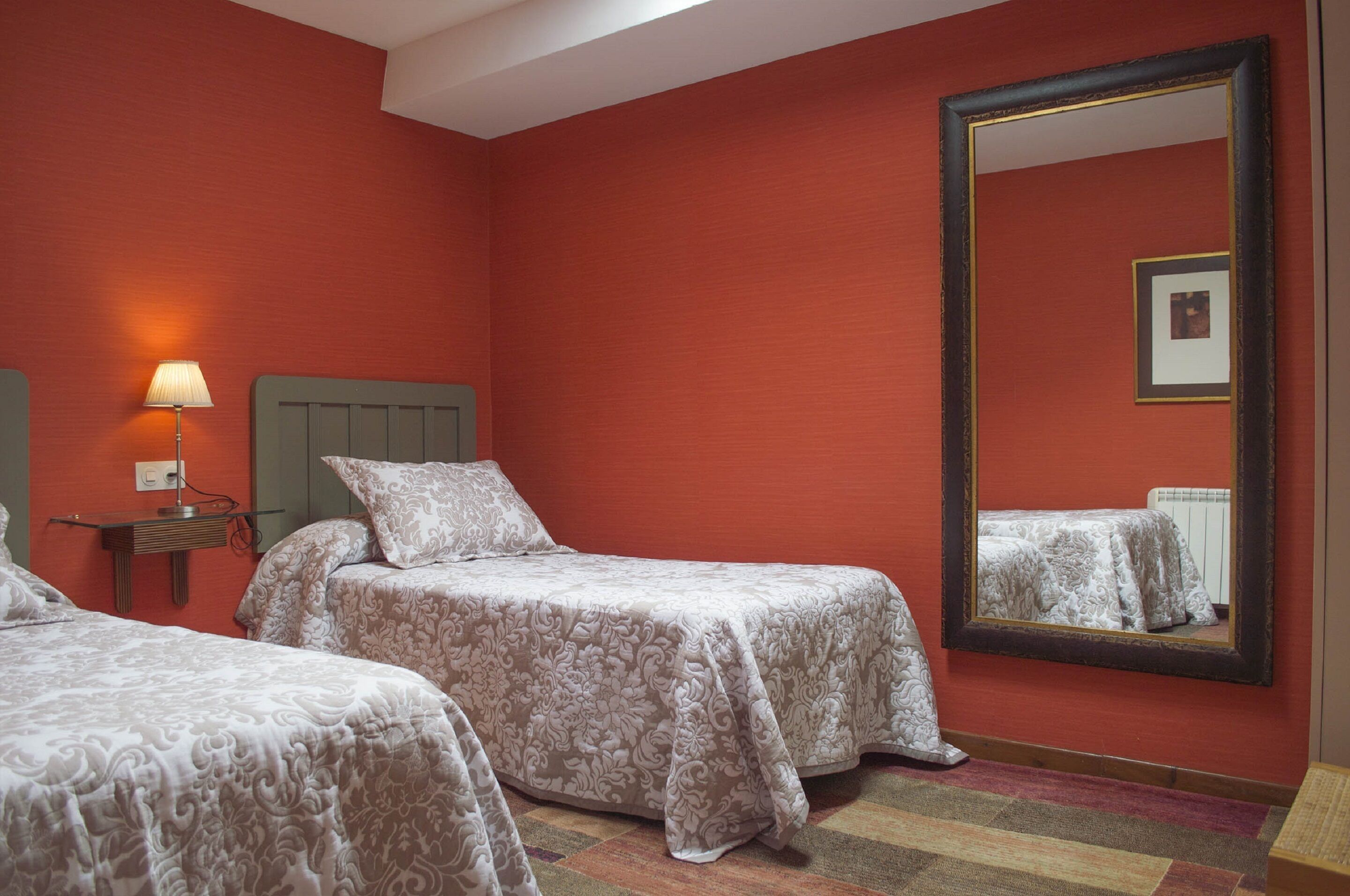 A hotel room with two beds, a nightstand with a lamp, a large mirror, and a framed picture on the wall.