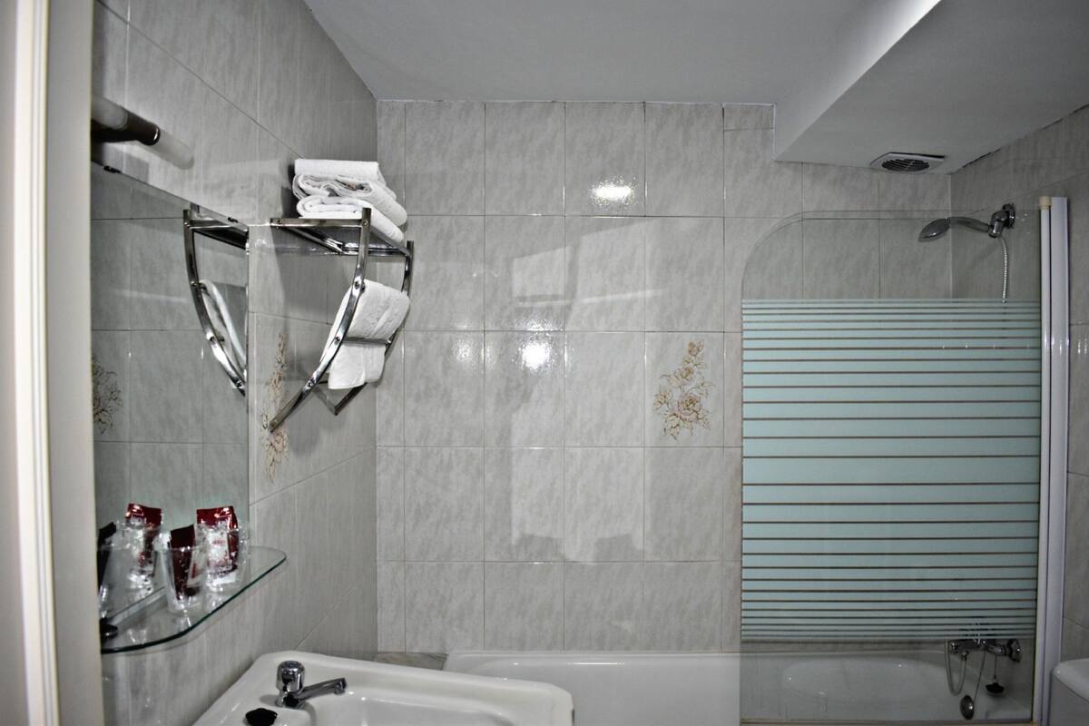 Un baño moderno con cabina de ducha de vidrio, estante de vidrio con artículos de aseo y una bañera blanca.