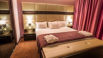 Habitación de hotel con una cama grande, cabecera con panel de luz, mesita de noche con lámpara y cortina roja.