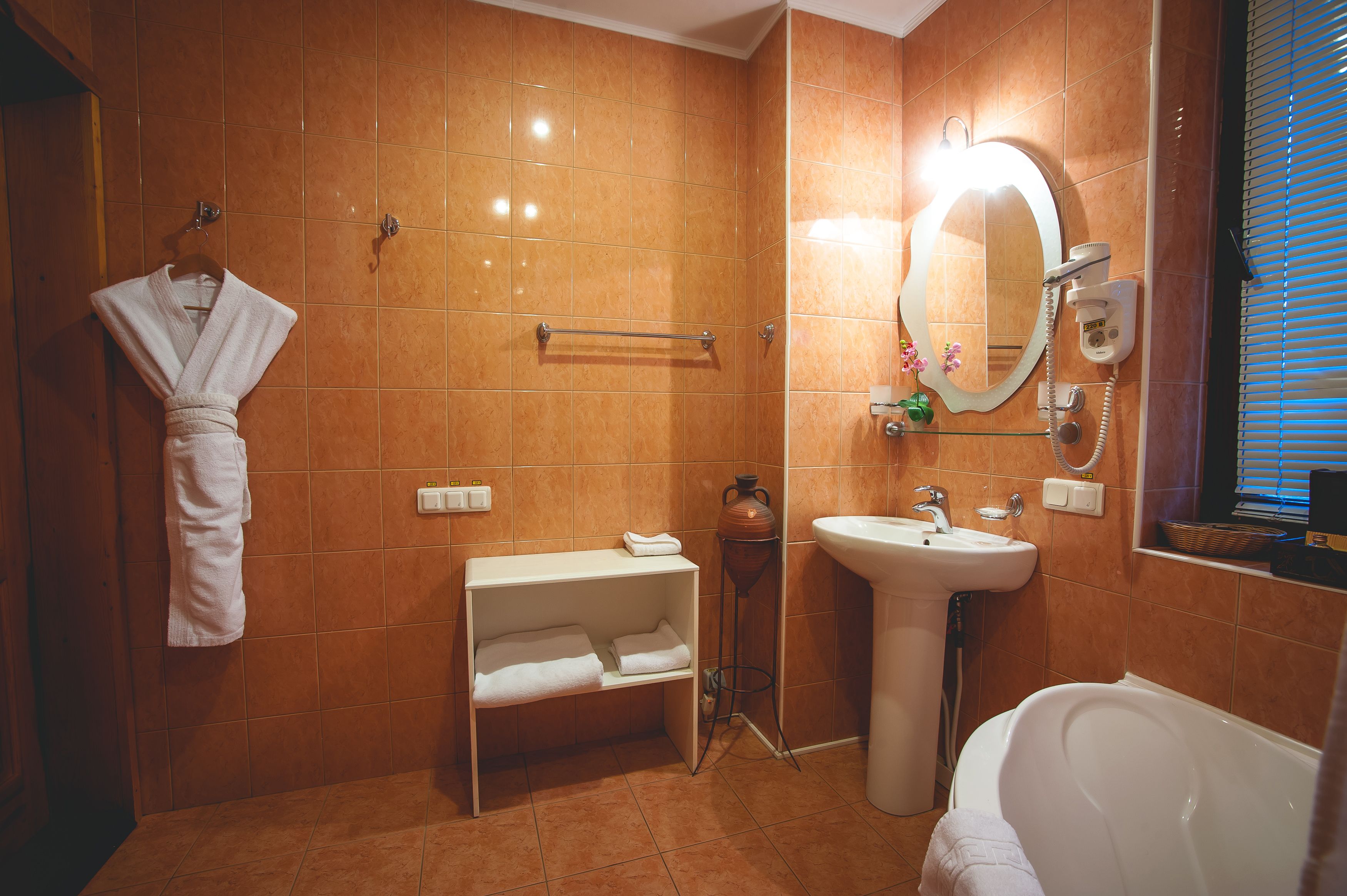 A bathroom with a bathtub, sink, mirror, towel rack, and a robe hanging on the wall.