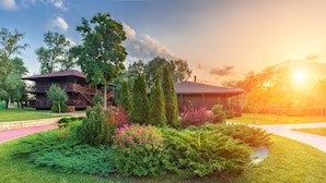 A building with a balcony and a covered area, surrounded by well-maintained greenery and a pathway.