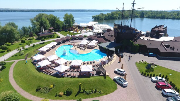 An aerial view of a resort with a central swimming pool, outdoor seating, and a large ship replica.