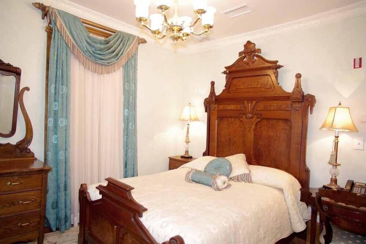 A classic four-poster bed with a wooden headboard, two bedside lamps, and a chandelier.