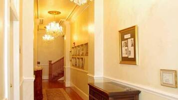 A hallway with a wooden floor, a patterned rug, a dark wooden bench, and a chandelier.