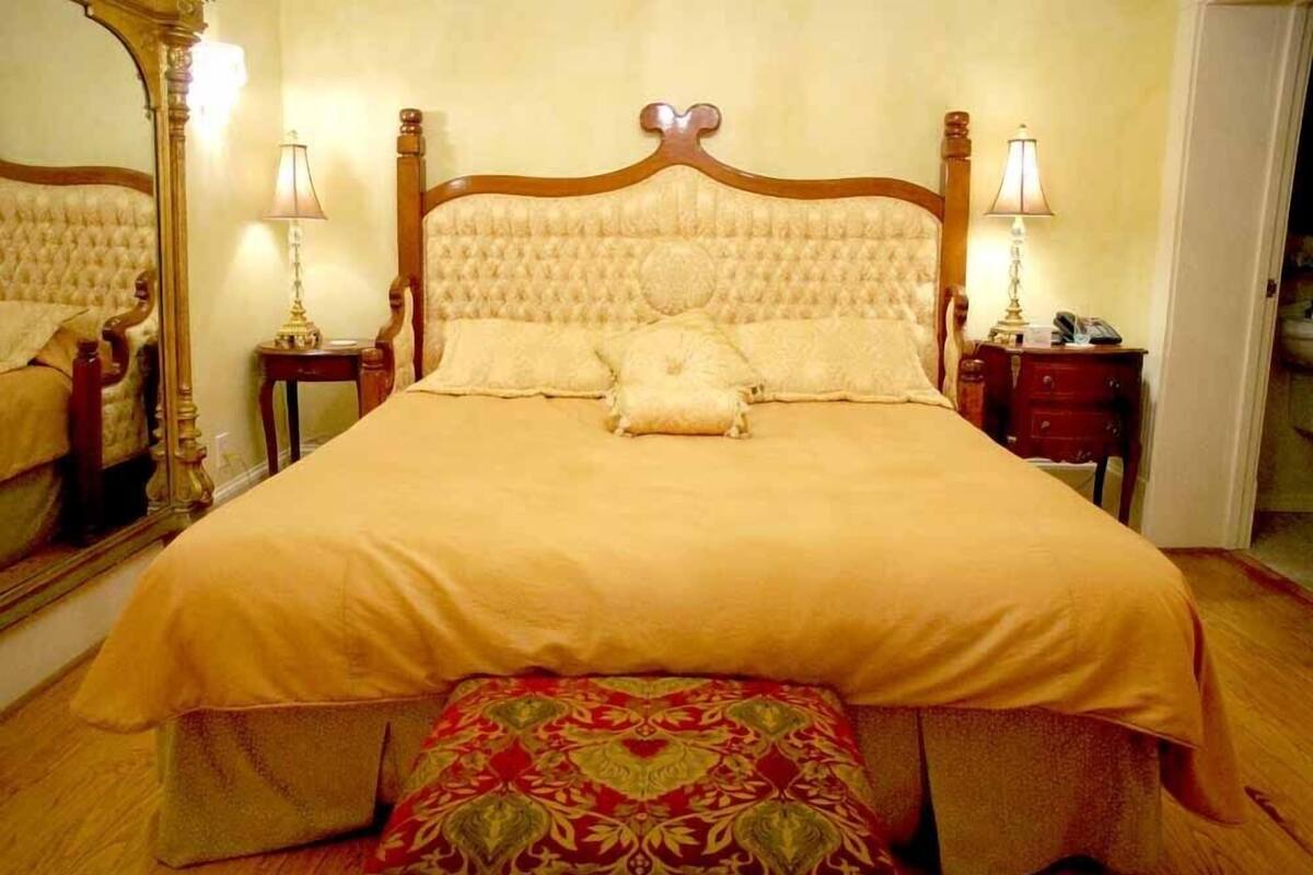 A large bed with a wooden headboard, two bedside tables with lamps, and a mirror on the wall.