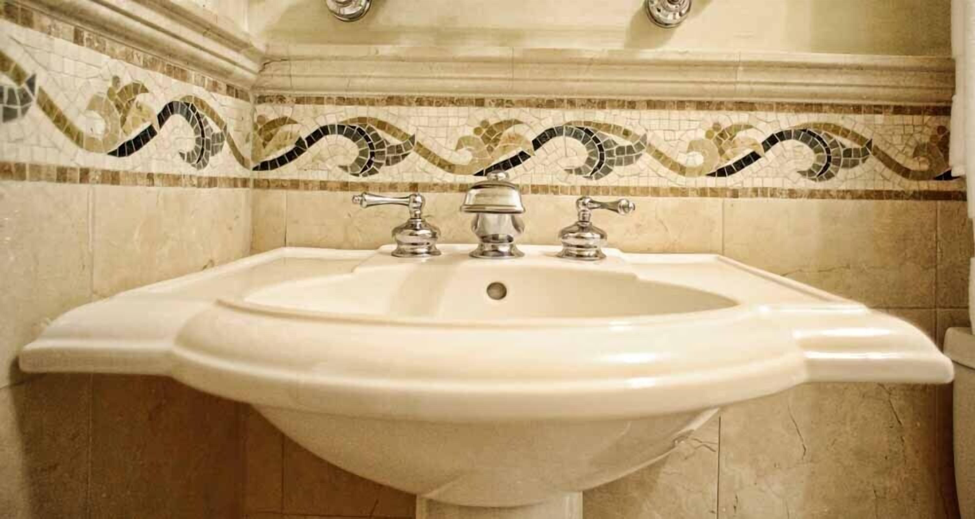 A bathroom sink with a mosaic tile backsplash and a marble wall.