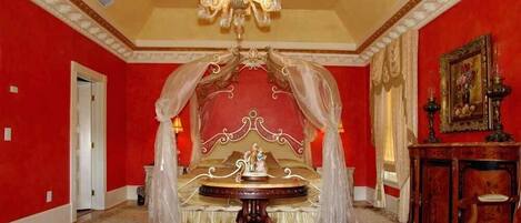 A room with a large bed, a chandelier, and a red wall.