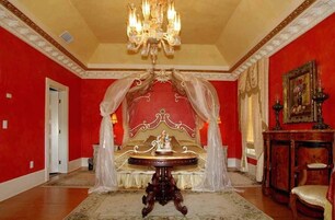 A room with a large bed, a chandelier, and a red wall.