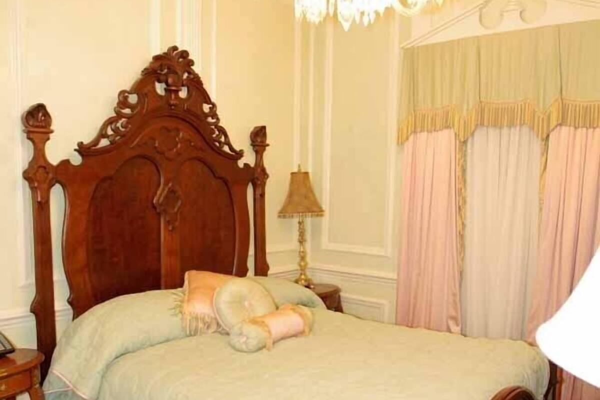 A classic four-poster bed with a wooden headboard, a chandelier, and a floral-patterned bedspread.