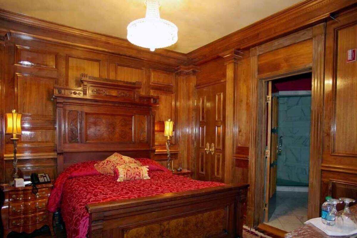 A wooden-paneled bedroom with a large bed, two bedside lamps, and a chandelier.