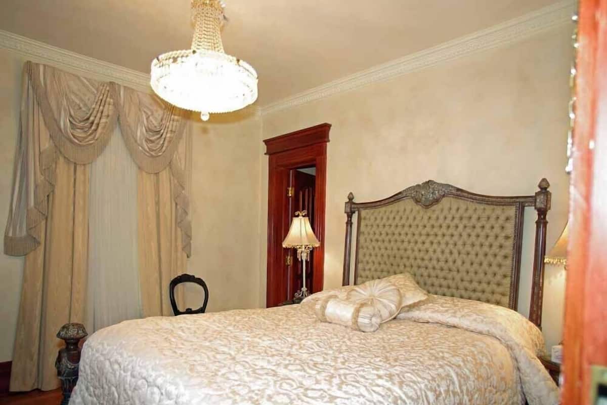 A bedroom with a large bed, a chandelier, and curtains.