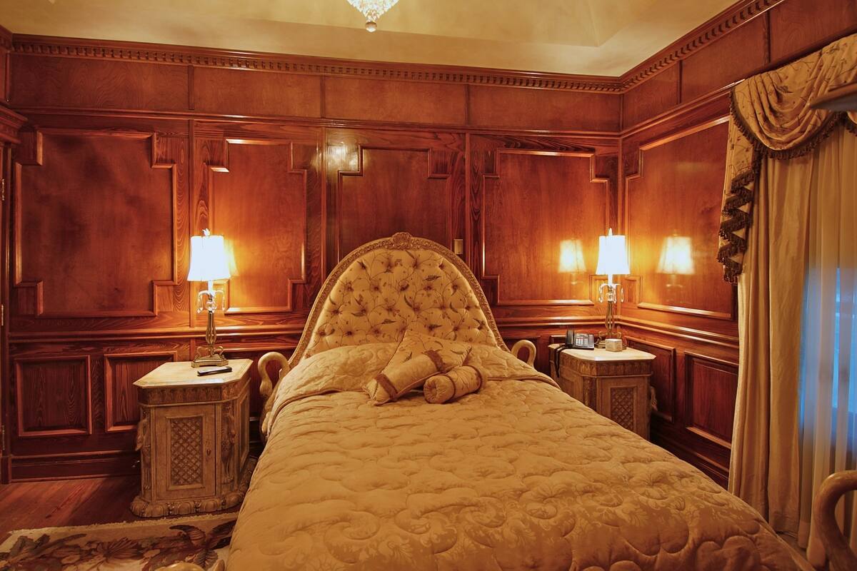 A large, ornate bed in a room with wooden paneling and two bedside lamps.