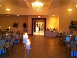 A banquet hall with round tables and chairs, a chandelier, and a door leading to another room.