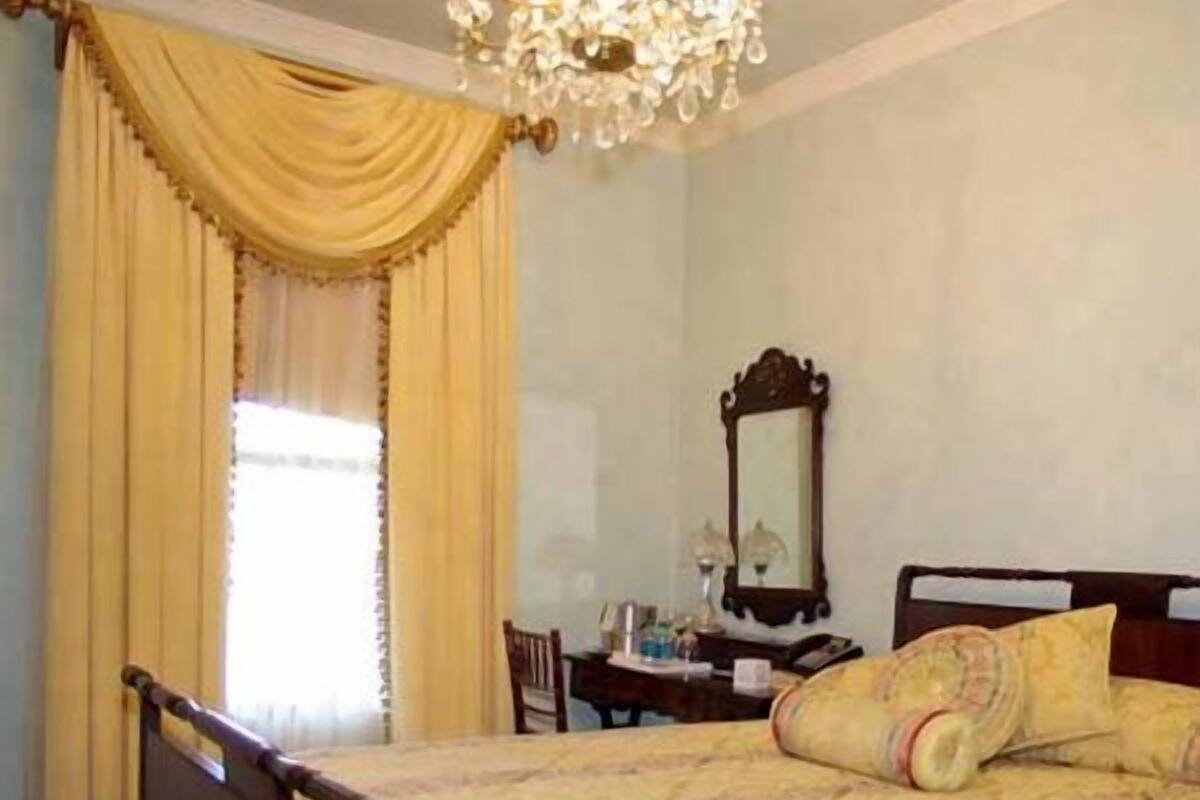 A bedroom with a wooden bed, a chandelier, a desk with a chair, and a window with curtains.