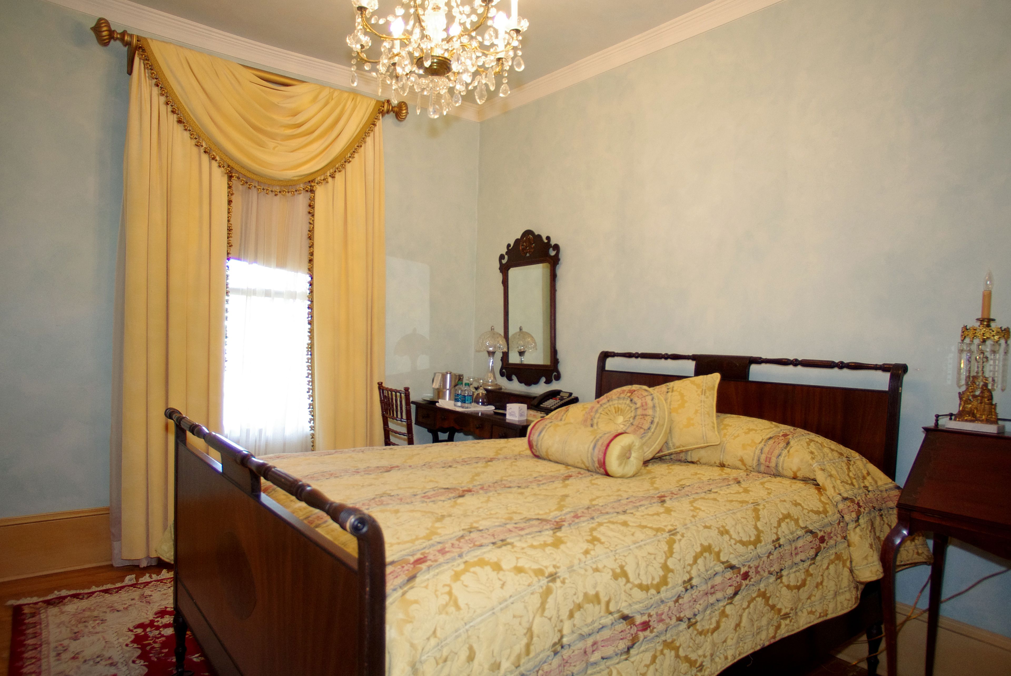 A bedroom with a wooden bed, a chandelier, a mirror, and a desk with a lamp.