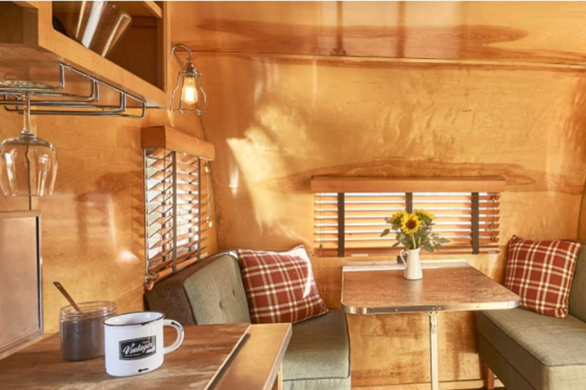 A cozy cabin interior with wooden walls, a dining table with a vase of sunflowers, and two cushioned seating areas.
