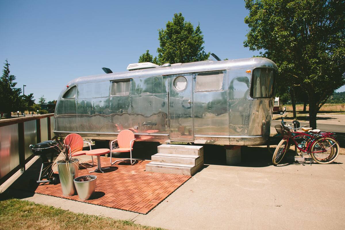 A vintage trailer with a patio area, including a grill, chairs, and a bicycle.