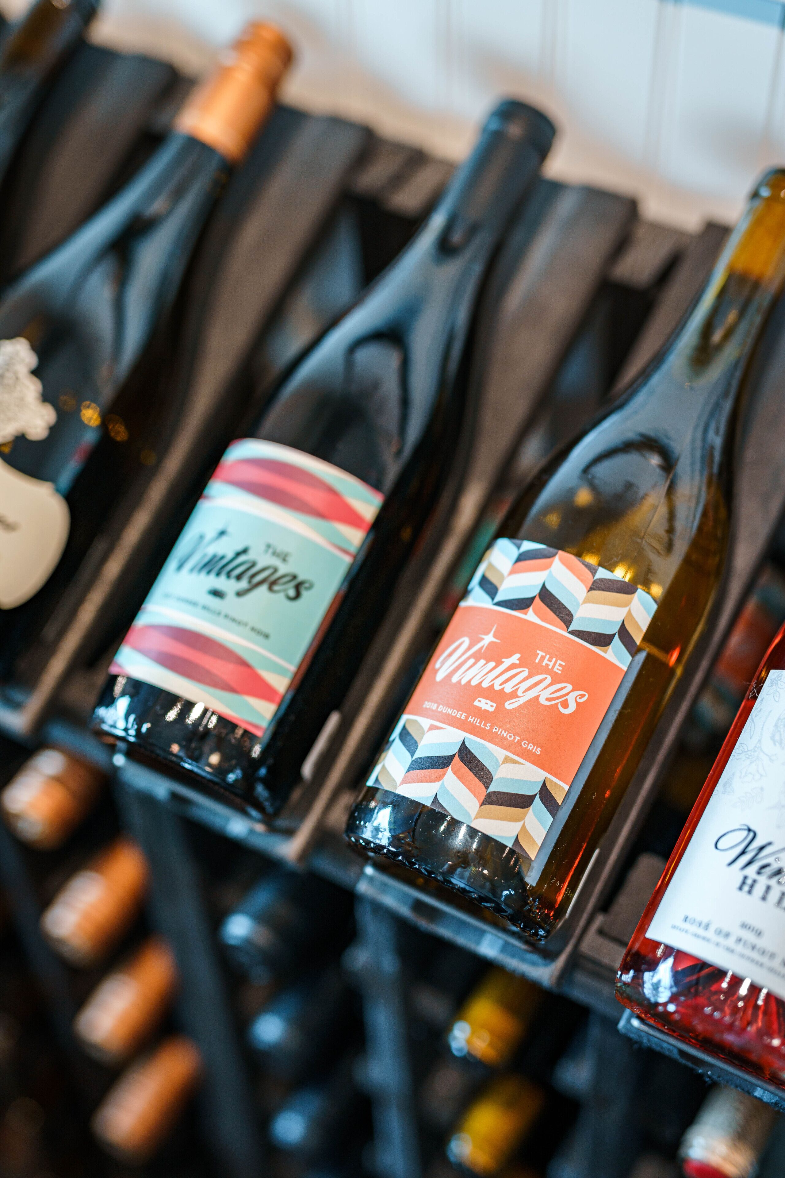 Una fila de botellas de vino con etiquetas, algunas con corchos, y una copa de vino a la izquierda.