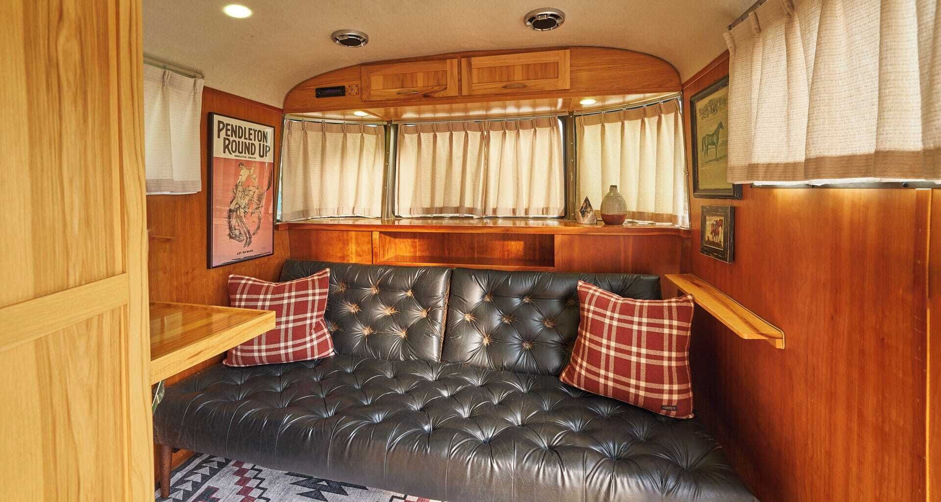 A cozy RV interior with a tufted leather sofa, wooden cabinets, and a window with curtains.
